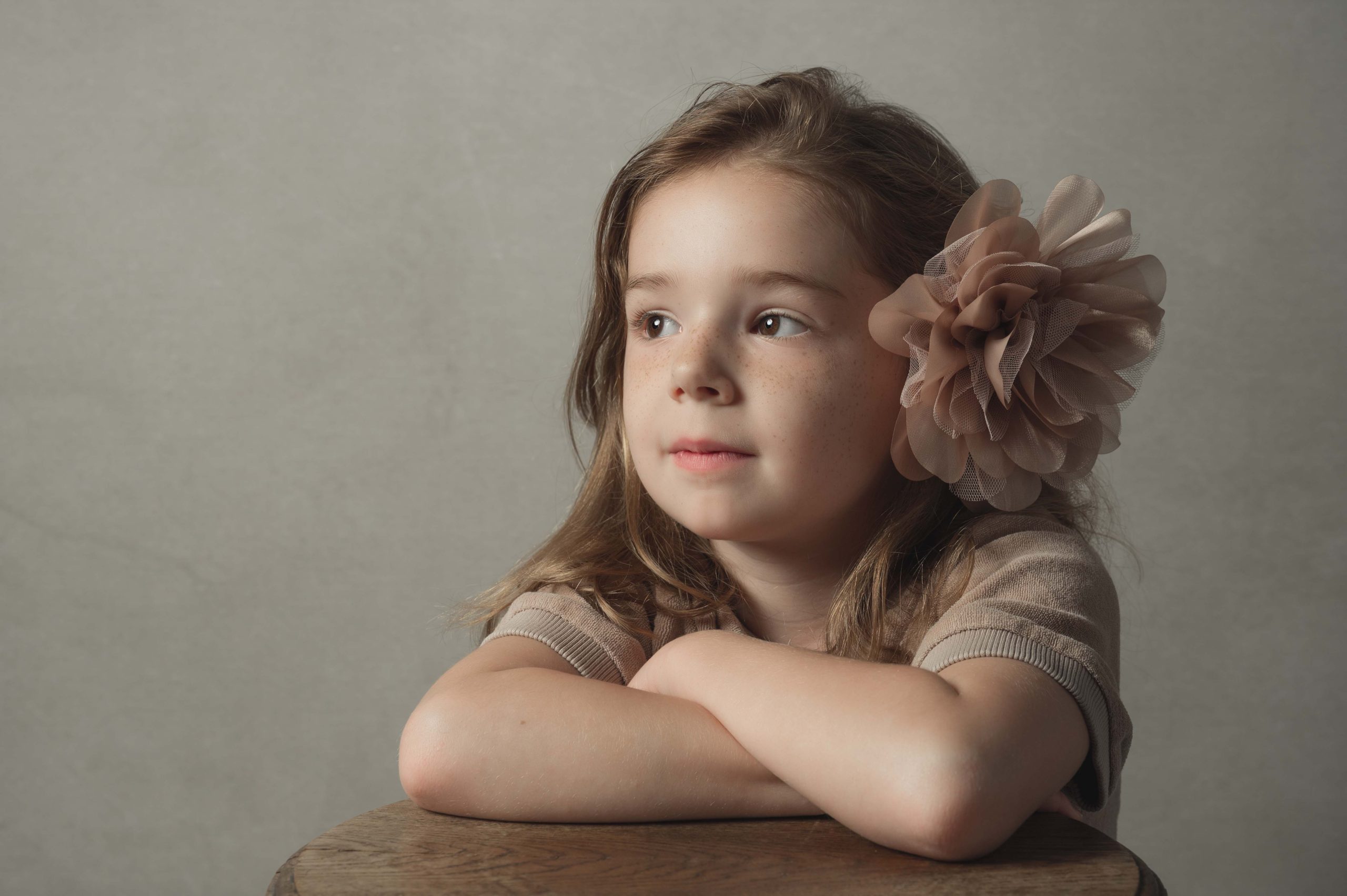 Fine art portret van een meisje met grote bloem in het haar tegen een rustige lichte achtergrond